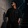 Zane Mode Tee by Multiversity in Jet Black Pantone Black C, featuring a minimal cyan chest logo and oversized 240 GSM cotton fit.